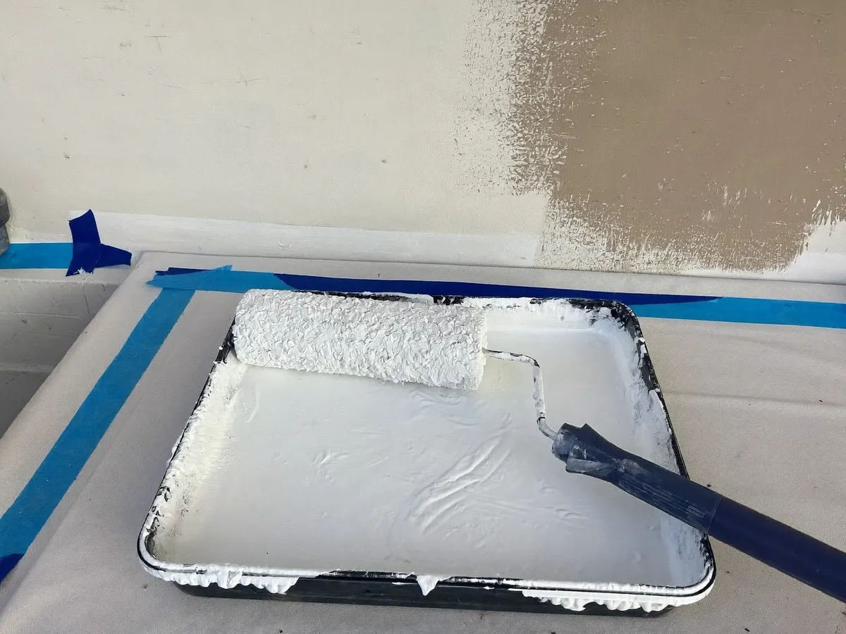 Paint roller in a tray of fresh white paint next to a half-painted villa wall